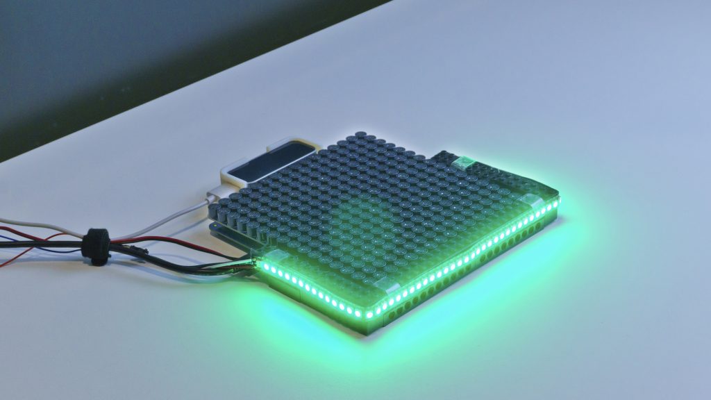 A photograph of the HaptiGlow device. An Ultrahaptics UHEV1 device with a strip of Adafruit NeoPixel LEDs positioned around the front edges of the haptics device.